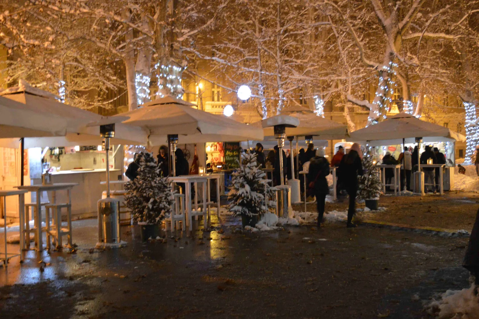 Snow-dusted Christmas market cabins and visitors under illuminated trees in Zagreb