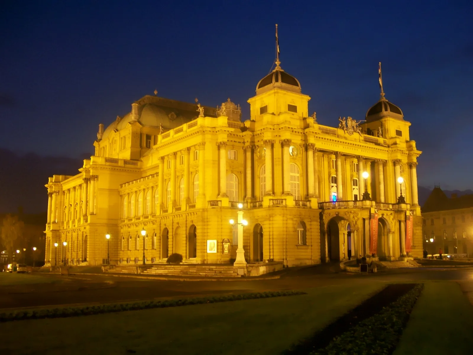 Croatian National Theatre illuminated gold at night beneath a dark blue sky