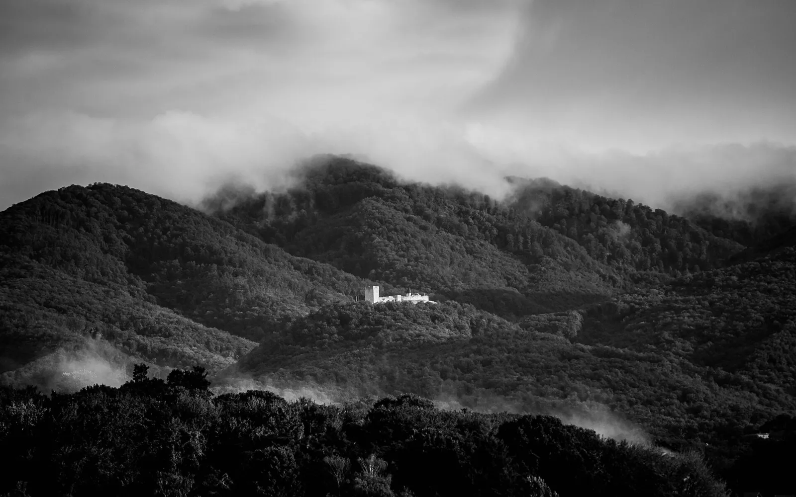 Small white Medvedgrad fortress visible against dark forested Medvednica ridges and low cloud