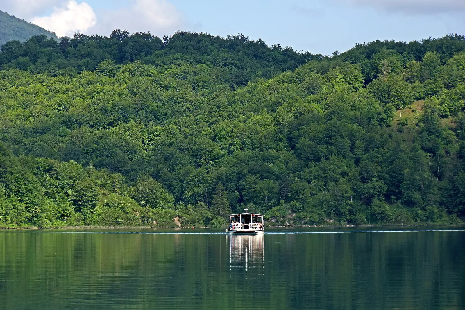 A small electric tourist boat crossing calm Kozjak Lake at Plitvice