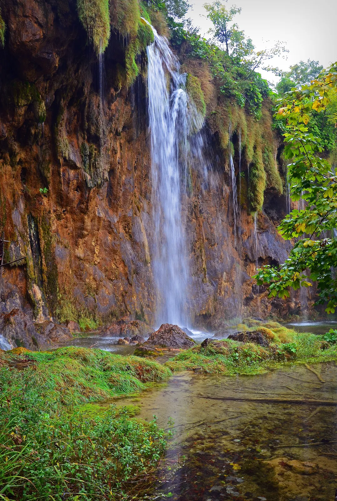 A tall waterfall dropping into clear water among moss and forest in the Upper Lakes