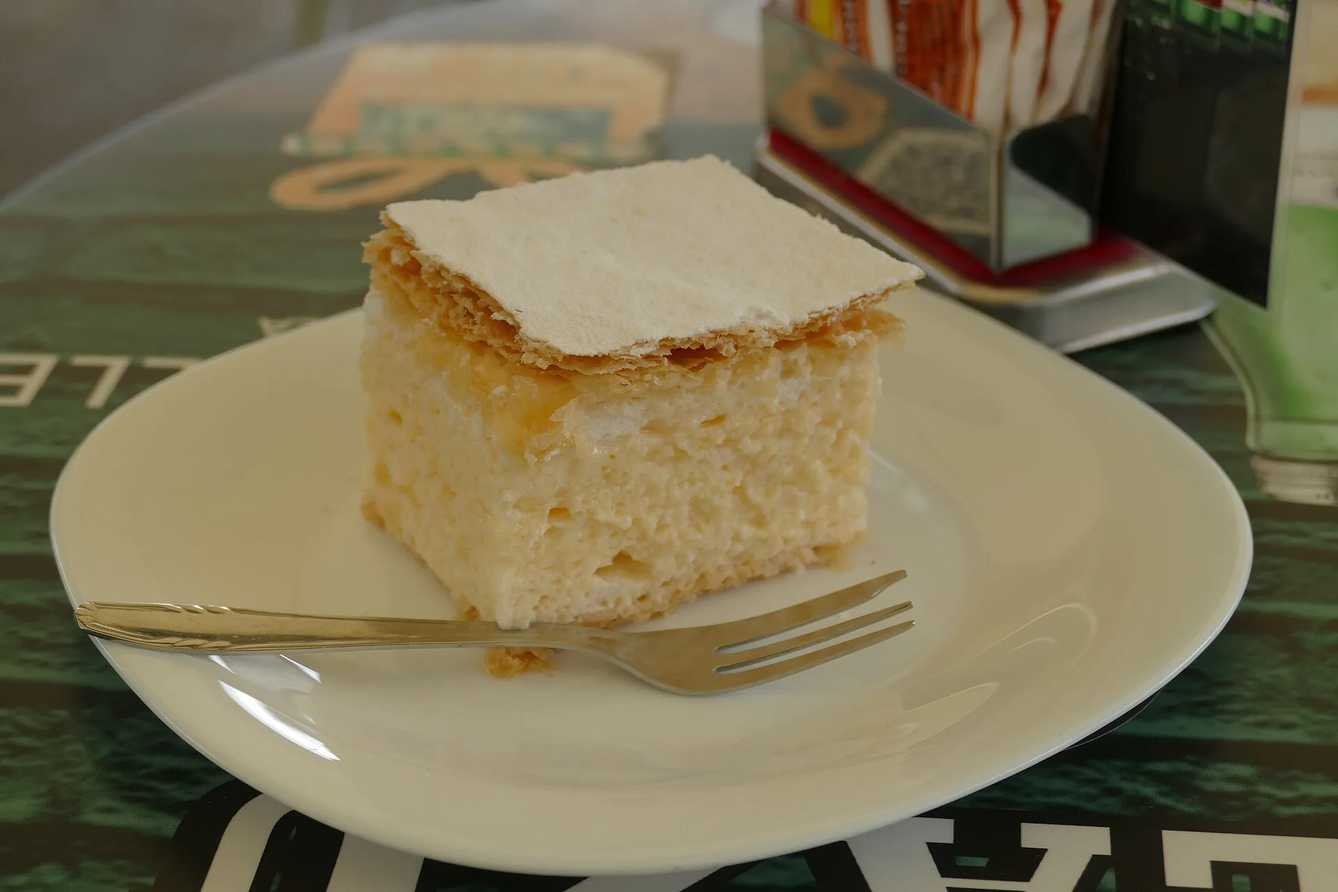A square slice of Samobor kremšnita dusted with sugar on a café plate