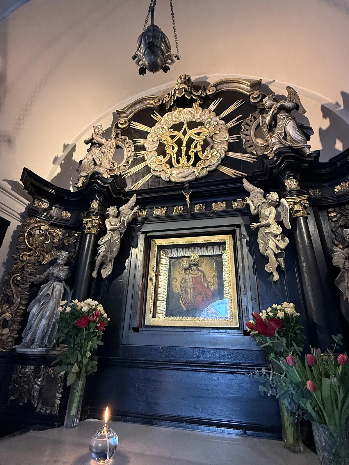Venerated Marian icon, carved dark altar and flowers inside Stone Gate