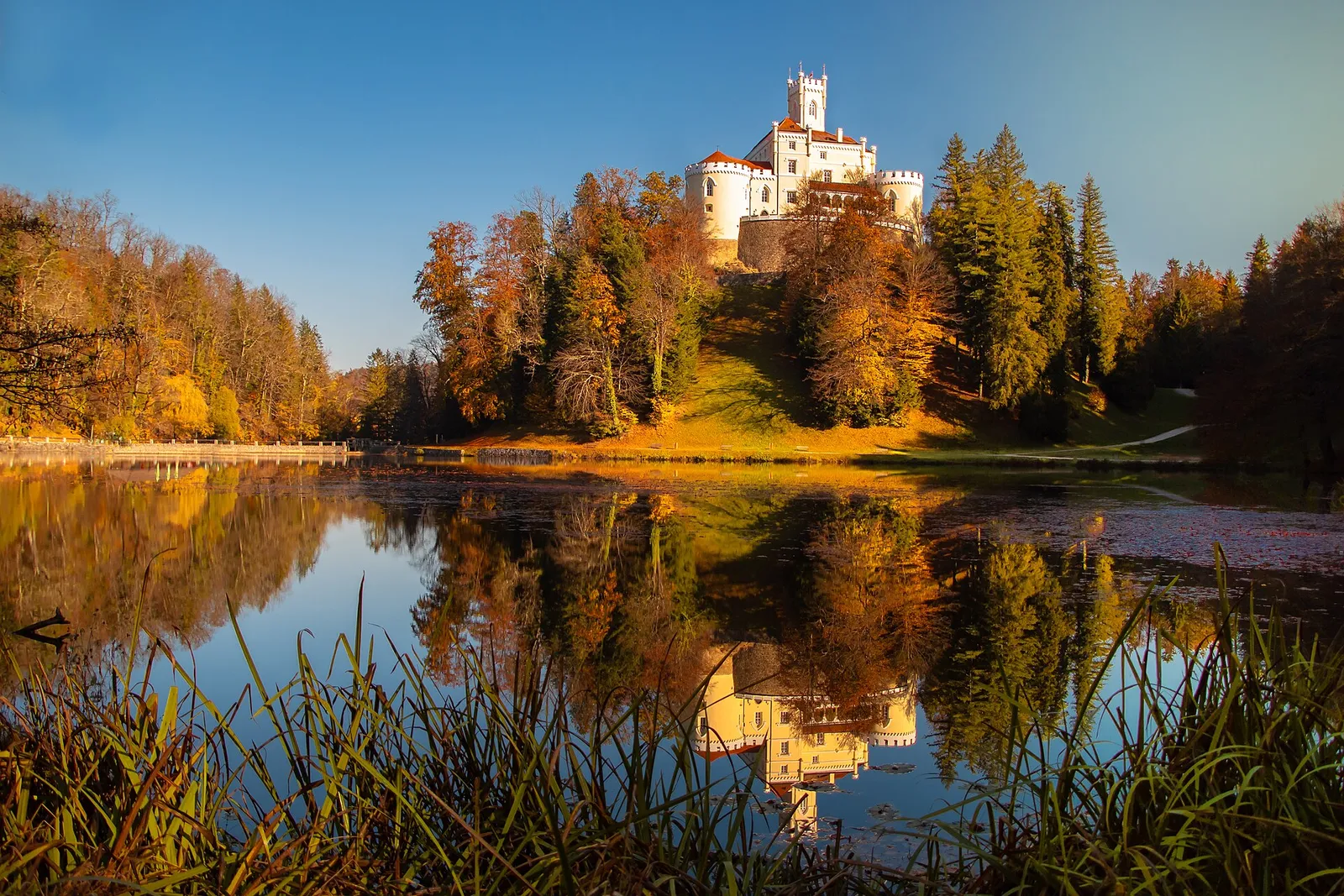 Trakošćan Castle above autumn forest with its reflection in still lake water