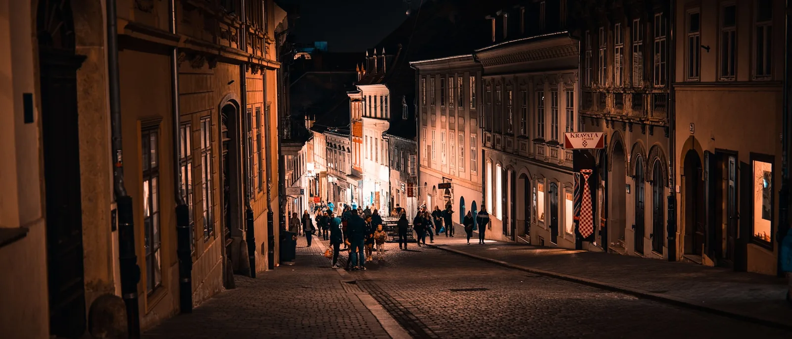 People walking down a cobbled Zagreb street after dark